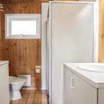 Badezimmer mit Toilette, Dusche und Waschbecken. Holzwände und Fliesenboden.