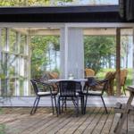 Terrasse mit Tisch und Stühlen vor einem Haus mit großem Fenster.