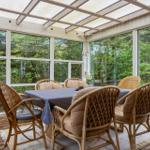 Draußenbereich mit Esstisch und Stühlen, großflächige Fenster, Blick auf grüne Umgebung.