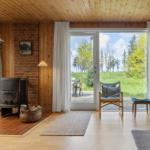 Wohnraum mit Holzwand, Kaminofen und großem Fensterblick auf Grünland.