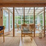 Haus mit Holzdecke, Glasfront und Terrasse mit Sitzgelegenheiten.