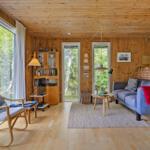 Wohnzimmer mit Holzdecke, Sofa, Sessel und großem Fenster zur Natur.