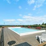 Pool mit Holzterrasse und Meerblick. Rote Bänke und weiße Liegestühle.