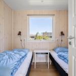 Zwei Betten mit blauen Decken, Holzwände, Fenster und Nachttisch.