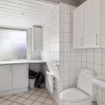 Badezimmer mit Toilette, Waschbecken und Fenster. Weiße Fliesen und Schränke.