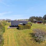 Modernes Haus mit Terrasse, umgeben von Grünfläche und Bäumen unter blauem Himmel.