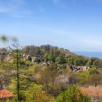 Haus mit rotem Dach, Blick auf Hügel und Meer unter blauem Himmel.