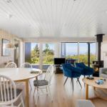 Wohn- und Essbereich mit Holzwänden, großen Fenstern und einem Kamin.