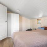 Schlafzimmer mit Bett, Kleiderschrank und Fenster. Holzwände und weißer Deckenverkleidung.