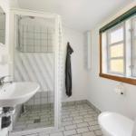 Badezimmer mit Dusche, Waschbecken und Toilette. Fenster mit Holzrahmen.