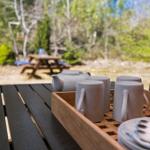 Außentisch mit Tee- und Geschirrset vor Wald im Hintergrund.