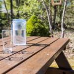 Holztisch mit Wassergläsern und Wasserkaraffe im Garten.