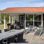 Terrasse mit Tischen, Stühlen und Liegen. Haus mit rotem Dach und Glasfront.