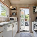 Küche mit Fenster, Tür zum Balkon und weißen Schränken.