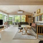 Wohnzimmer mit Holzwand, Sofa, Tisch und Fernseher. Große Fenster mit Blick auf Grün.