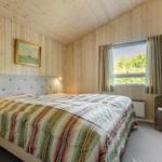 Schlafzimmer mit Holzwand, Bett, Fenster und Stuhl.