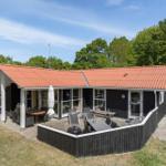 Haus mit Terrasse, Grill und Garten. Umgeben von Bäumen unter blauem Himmel.