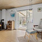 Living room with wooden ceiling, wood stove, and armchair. Door leads to terrace.