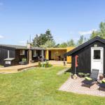 Schwarze Holzhäuser mit Terrasse und Garten. Liegestühle und Pflanzen sind vorhanden.