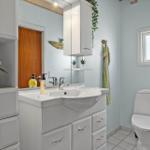 Badezimmer mit Waschbecken, Spiegel, Toilette und Fenster.