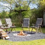 Feuerstelle mit vier Liegestühlen im Garten. Holzstapel und Baumhaus im Hintergrund.