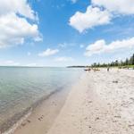 Strand mit klarem Wasser und Sand, einige Personen und ein Haus im Hintergrund.