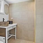 Badezimmer mit Waschtisch, Spiegel und Toilette. Wandfliesen und Holzelemente.