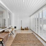 Lange Halle mit weißen Wänden, Holzboden und großen Fenstern mit Jalousien.