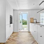 Moderne Küche mit weißer Einbauküche, Holzboden und Blick auf den Garten.