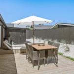 Terrasse mit Tisch, Stühlen und Sonnenschirm neben Haus mit Holzdecke und Sandhügel.