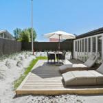 Terrasse mit Liegestühlen, Tisch und Sonnenschirm neben einem Haus mit Fenstern.