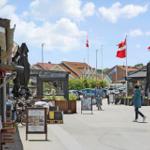 Straßenszene mit Flaggen, Geschäften und Passanten unter blauem Himmel.