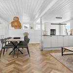 Wohn- und Essbereich mit Holzboden, weißer Küche und Esstisch mit Stühlen.