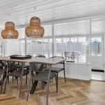 Esszimmer mit Holztisch, Stühlen und hängenden Lampen. Durchgang zur Terrasse mit Fenstern.