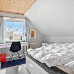 Schlafzimmer mit Dachschräge, Bett, Schreibtisch und Fenster.