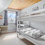 Zimmer mit Doppelstockbett, Fenster, Vorhängen und Stuhl mit Plüschfigur.