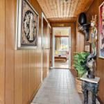 Flur mit Holzwand, Kunstwerken und Pflanze. Durchgang in Wohnzimmer mit Sofa.