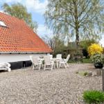 Hinterhof mit Tisch, Stühlen, Steinfigur und Grasfläche unter blauem Himmel.