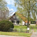 Haus mit Garten, Terrasse und Bäumen unter blauem Himmel.