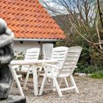 Garten mit weißem Tisch und Stühlen, Steinfigur und rotem Dach im Hintergrund.