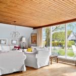 Wohnzimmer mit Holzdecke, weißen Sofas und großem Fensterblick auf Garten