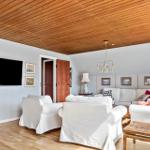 Wohnzimmer mit weißen Sesseln, Fernseher und Holzdecke.