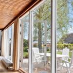 Wohnzimmer mit Holzdecke und großem Fenster zur Terrasse mit weißen Stühlen.