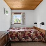 Schlafzimmer mit Holzdecke, Bett mit gemusterter Bettdecke und Fenster mit Vorhängen.