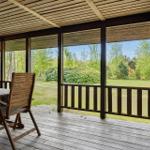 Terrasse mit Holztisch und Stuhl, Blick auf Grünfläche und Bäume.