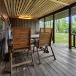 Holzterrasse mit Tisch und Stühlen, Blick auf grüne Wiese und Bäume.
