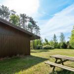 Holzhaus mit Picknicktisch im Garten unter Bäumen.