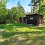 Hinterhof mit Holzhaus, Grillplatz und grünem Rasen im Wald.