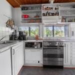 Küche mit weißen Schränken, Edelstahlherd und Fenstern zum Garten.