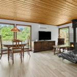 Wohn- und Essbereich mit Holzdecke, Kamin und TV. Holzmöbel und große Fenster.